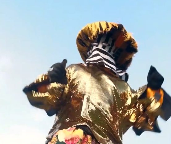 Performer in gold sequined costume and striped mask